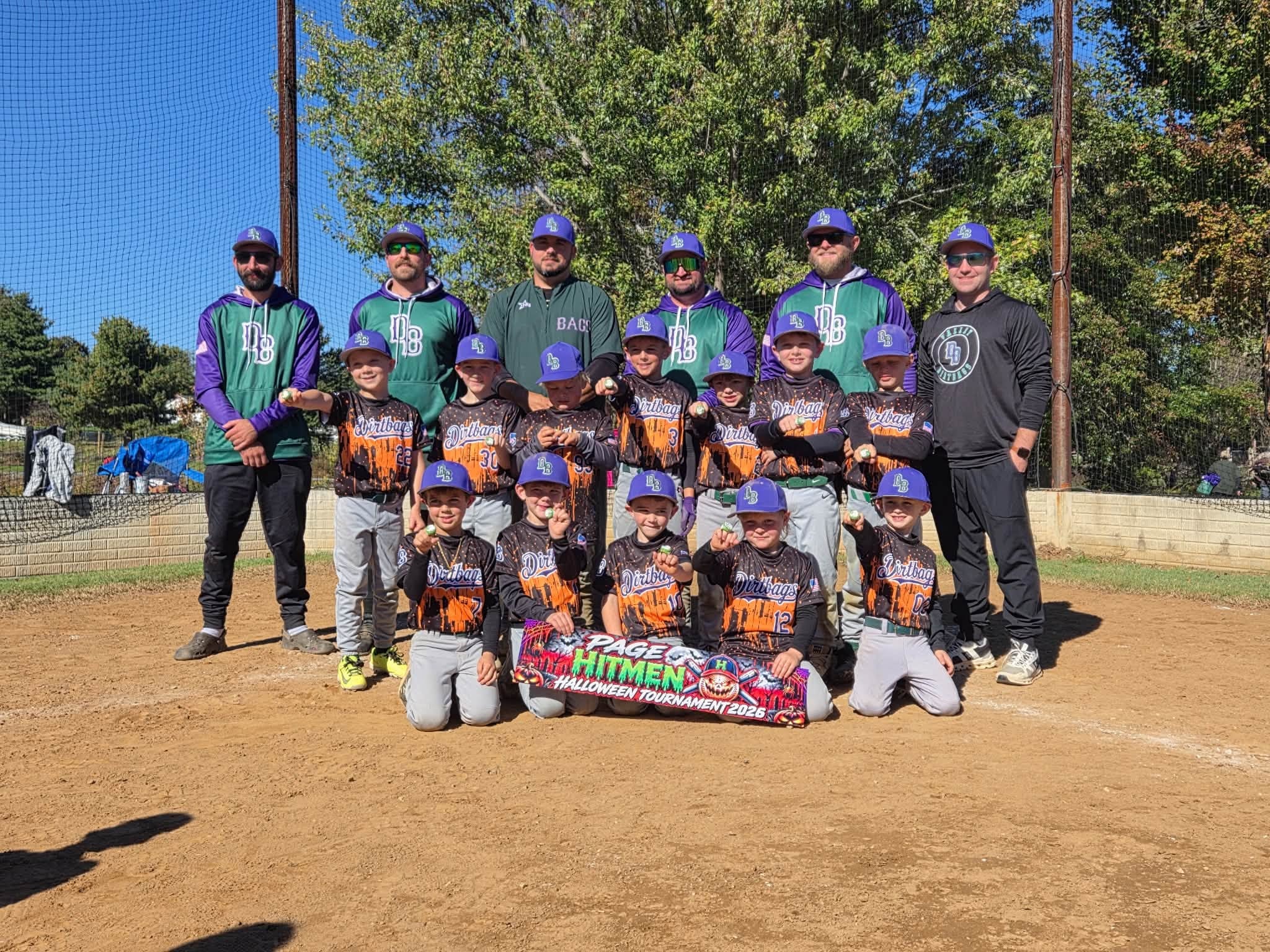 Dirtbags players and coaches posing with a tournament banner on the infield